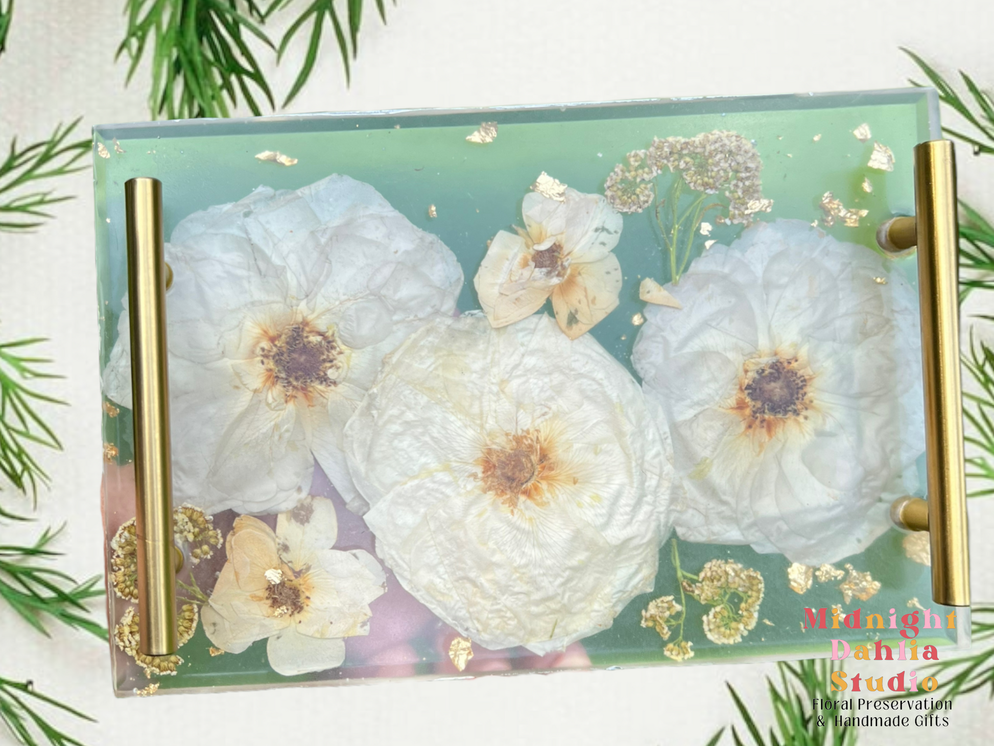 A custom serving tray with pressed flowers white roses and gold flakes .  It has gold handles and is made of crystal clear resin.